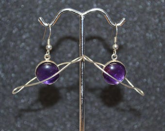 Puede incluir: Un par de pendientes de plata con una piedra de amatista púrpura engastada en un anillo de plata que se asemeja a un planeta con un anillo alrededor.