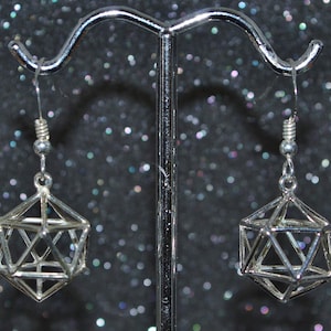 May include: A pair of silver geometric dangle earrings with a cage-like design. The earrings are hanging from a silver stand.