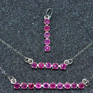 May include: Three silver necklaces with pink gemstone accents. The top necklace features a pendant with a vertical row of gemstones. The middle necklace has a curved row of gemstones. The bottom necklace has a straight row of gemstones.
