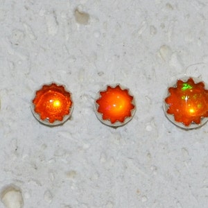 May include: Five pairs of orange opal earrings in different sizes. The earrings are set in silver and have a starburst design.