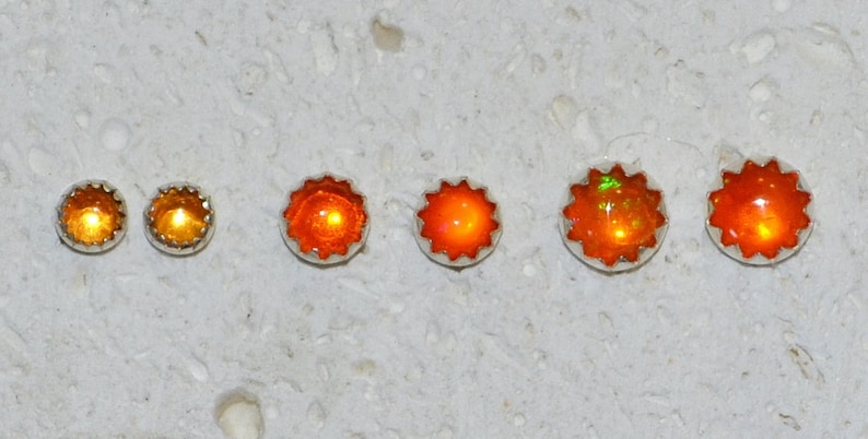 May include: Five pairs of orange opal earrings in different sizes. The earrings are set in silver and have a starburst design.