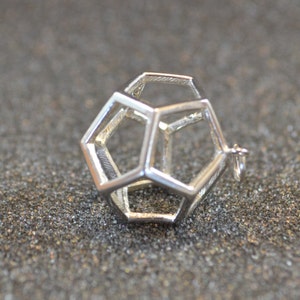 Peut inclure: Un pendentif g&eacute;om&eacute;trique argent&eacute; avec un design creux en forme de cage. Le pendentif est en m&eacute;tal et a une finition lisse et polie.