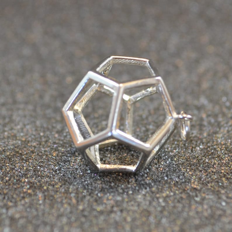 Peut inclure: Un pendentif g&eacute;om&eacute;trique argent&eacute; avec un design creux en forme de cage. Le pendentif est en m&eacute;tal et a une finition lisse et polie.