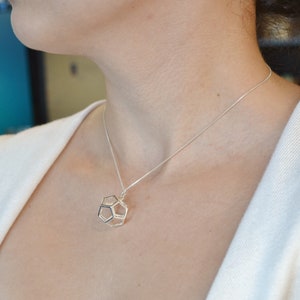 Peut inclure: Un collier en argent avec un pendentif g&eacute;om&eacute;trique. Le pendentif est une forme tridimensionnelle avec un motif hexagonal.