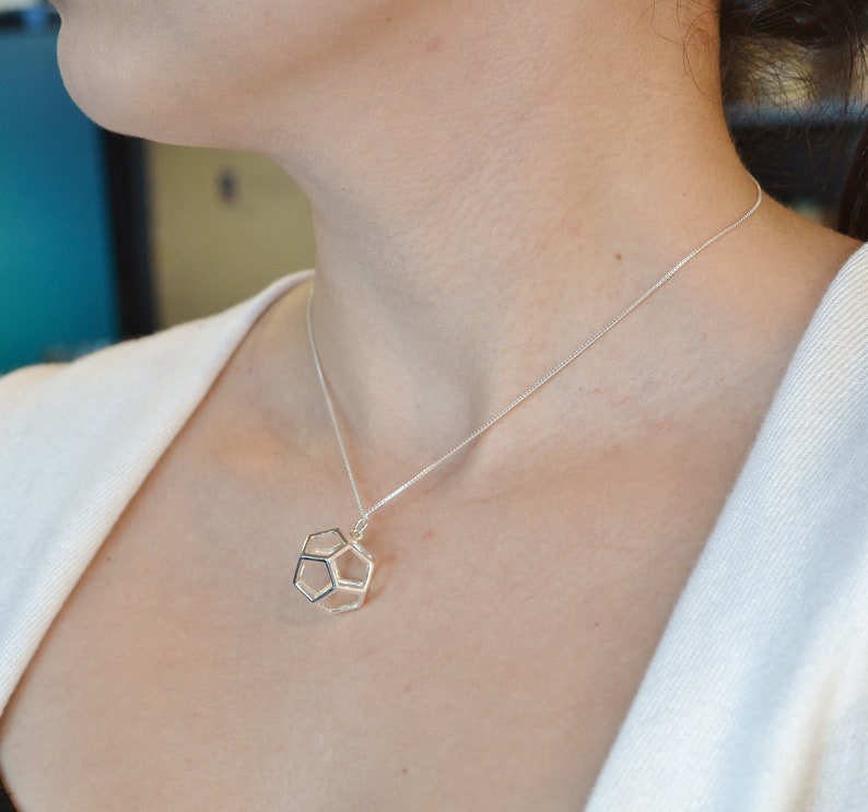 Peut inclure: Un collier en argent avec un pendentif g&eacute;om&eacute;trique. Le pendentif est une forme tridimensionnelle avec un motif hexagonal.