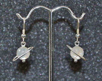 May include: A pair of silver dangle earrings with a white moonstone sphere and a silver ring around it, resembling a planet with a ring.