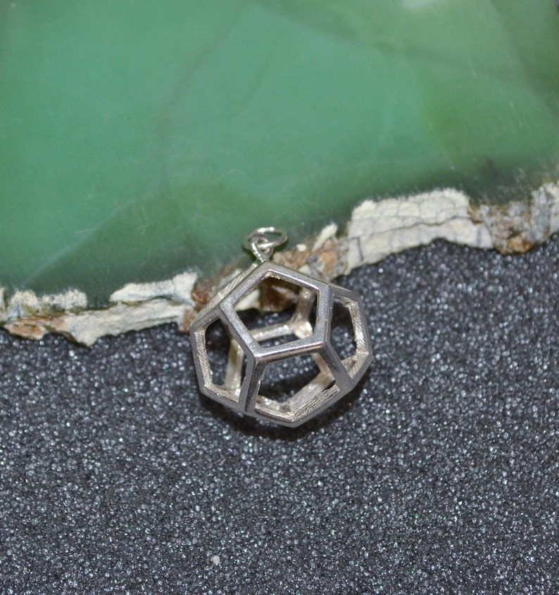 Peut inclure: Un pendentif en argent de forme g&eacute;om&eacute;trique, en forme de dod&eacute;ca&egrave;dre. Le pendentif est creux et pr&eacute;sente un design en fil de fer.