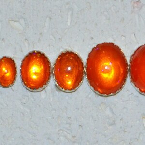 May include: Five orange opal cabochons of varying sizes, set in silver bezels with scalloped edges.