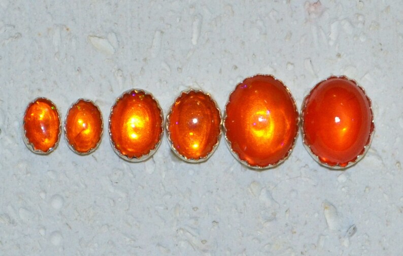May include: Five orange opal cabochons of varying sizes, set in silver bezels with scalloped edges.
