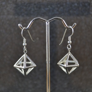 May include: A pair of silver geometric dangle earrings with a diamond-shaped design. The earrings are hanging from a silver stand.