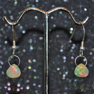 May include: A pair of silver dangle earrings with teardrop-shaped opal stones. The opals have a white base with flashes of green, orange, and red.