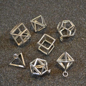 Puede incluir: Un conjunto de nueve colgantes geom&eacute;tricos de plata, que incluyen un cubo, una pir&aacute;mide y otras formas. Los colgantes est&aacute;n hechos de alambre y tienen un aspecto delicado y aireado.