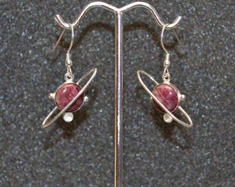May include: A pair of silver earrings with a pink and white gemstone in the shape of a planet with a silver ring around it.