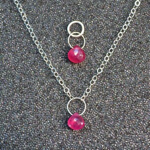 May include: A silver chain necklace with two pink gemstone pendants. The pendants are heart-shaped and hang from silver rings.