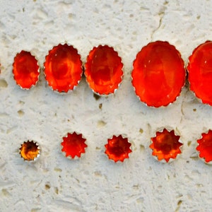 May include: A set of ten orange and brown star-shaped earrings with a silver setting. The earrings are arranged in two rows on a white textured surface.