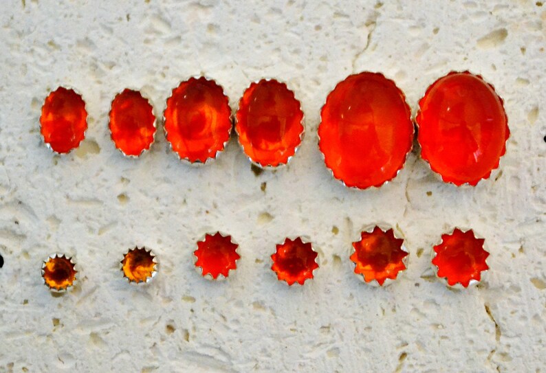 May include: A set of ten orange and brown star-shaped earrings with a silver setting. The earrings are arranged in two rows on a white textured surface.