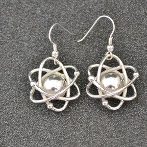 Pu&ograve; includere: Un paio di orecchini a forma di atomo in argento. Ogni orecchino presenta un atomo in argento con un centro rotondo e un gancio in argento.