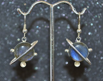 May include: A pair of silver earrings with a blue labradorite stone set in a silver ring with a smaller silver ring around it. The earrings are hanging from a silver hook.