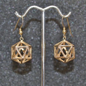 Peut inclure: Une paire de boucles d'oreilles pendantes géométriques dorées avec un design en fil. Les boucles d'oreilles sont suspendues à un support de boucles d'oreilles en argent.