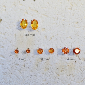 May include: A collection of stud earrings with orange gemstones in various sizes. The largest pair is oval-shaped, measuring 6x4 mm. Other pairs are round, with sizes ranging from 2 mm to 4 mm. All are set in silver.