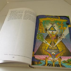 Peut inclure: Un livre ouvert avec une illustration color&eacute;e sur la page de droite. L'illustration pr&eacute;sente une pyramide, des personnages et une figure centrale aux bras lev&eacute;s. La page de gauche contient du texte imprim&eacute;. Le livre est intitul&eacute; "R&eacute;surrection au-del&agrave; de la Dualit&eacute; dans la Trinitisation Sainte".