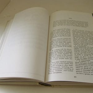 Peut inclure: Un livre ouvert avec du texte sur la page de droite et des pages vierges sur la gauche. Le livre a une reliure noire et une couverture de couleur claire. Le texte est en noir.