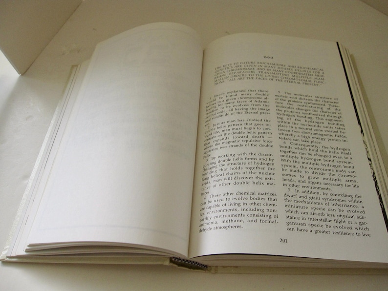 Peut inclure: Un livre ouvert avec du texte sur la page de droite et des pages vierges sur la gauche. Le livre a une reliure noire et une couverture de couleur claire. Le texte est en noir.