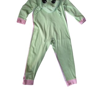 May include: Green and pink hooded onesie with a character from the Star Wars franchise, The Mandalorian, on the hood.