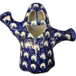 May include: A ceramic ghost figurine with outstretched arms, featuring a dark blue and white pattern. The ghost has a smiling face with two eye holes and a mouth opening. The design is reminiscent of Polish pottery.