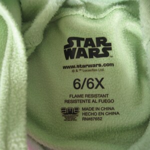 May include: Green Star Wars hooded sweatshirt with a tag that says "STAR WARS" and "www.starwars.com & TM Lucasfilm Ltd." The tag also says "6/6X", "FLAME RESISTANT", "RESISTENTE AL FUEGO", "MADE IN CHINA", "HECHO EN CHINA", and "RN#87652".