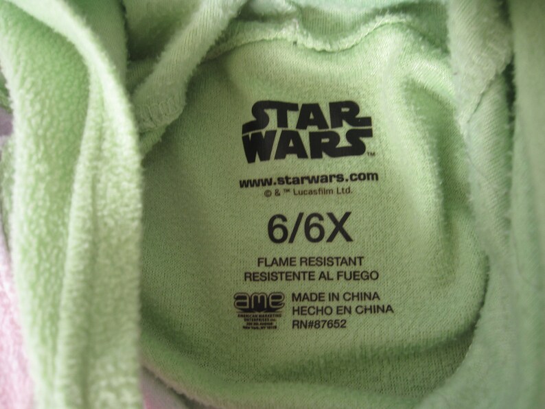 May include: Green Star Wars hooded sweatshirt with a tag that says "STAR WARS" and "www.starwars.com & TM Lucasfilm Ltd." The tag also says "6/6X", "FLAME RESISTANT", "RESISTENTE AL FUEGO", "MADE IN CHINA", "HECHO EN CHINA", and "RN#87652".