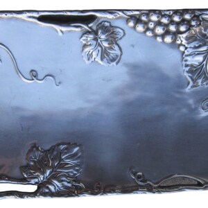 May include: A silver serving tray with a grapevine design. The tray is rectangular and has a raised edge. The grapevine design is embossed and includes leaves and grapes.