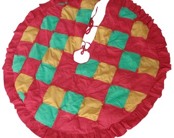 May include: A red, green, and gold quilted Christmas tree skirt with a ruffled edge. The skirt is tied in the center with a red ribbon.