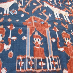 以下が含まれることがあります： 茶色、白、水色の濃淡で繰り返される模様の青い生地のクローズアップ。 デザインは、様式化された人物、動物、幾何学的な形を特徴とし、テクスチャード加工された芸術的な外観を作り出しています。 生地は綿または同様の素材のようです。