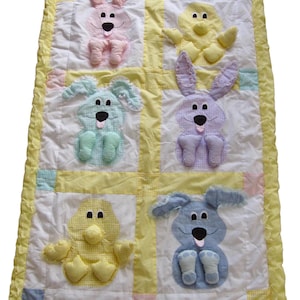 May include: A yellow, white, and pink baby quilt with appliqued animal designs. The quilt features a bunny, a duck, and a dog in each of the four squares. The quilt has a yellow border with a ruffled edge.