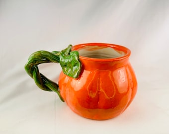 May include: Orange ceramic pumpkin mug with a green stem and leaf handle.