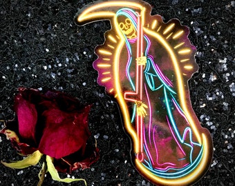 May include: A neon sticker of a skeleton figure holding a scythe, with a halo behind it. The figure is outlined in yellow, blue, and pink neon colors. The sticker is on a black background.