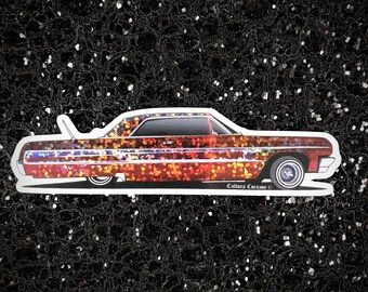May include: A red, orange, and yellow lowrider car sticker with a glittery finish. The sticker features a classic car with a white interior and chrome accents. The sticker has the text "Cultura Corazon" on the bottom.