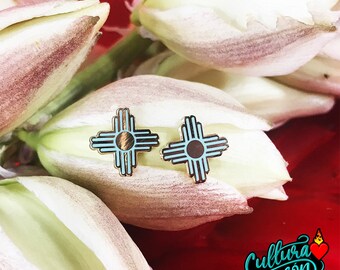 May include: A pair of turquoise blue and gold earrings with a Southwestern design. The earrings are shaped like a cross with a sun symbol in the center. The earrings are on a white background.