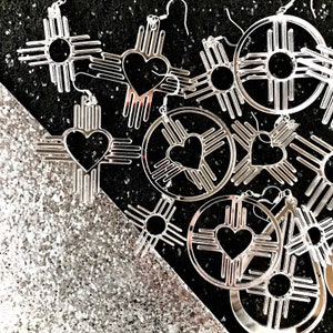 Peut inclure: Boucles d'oreilles argentées avec un motif de cœur et de soleil. Les boucles d'oreilles sont en forme de symbole amérindien traditionnel.