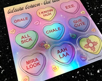 May include: A sheet of holographic stickers featuring heart-shaped candy with various phrases in Spanish and English, including "Que Cute Candy!" "Órale" "I Know Huh" "All Sick" "Mira Look" "EEE" "Chale" "Aah Laa" "Que Cute" and "CulturaCorazon."
