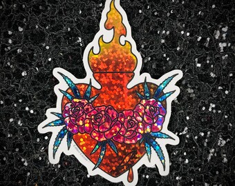 May include: A holographic sticker of a red heart with a flame on top, surrounded by pink roses and blue leaves. The heart is dripping red liquid. The sticker has a glitter finish.