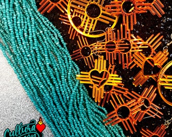 May include: A turquoise beaded necklace with multiple orange and brown sun symbol earrings. The earrings are in the shape of a sun with four points and a circle in the center. The earrings are layered on top of each other.