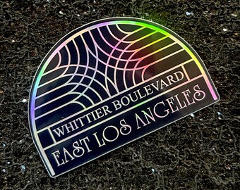 May include: A black and silver iridescent sticker with a geometric design and the text "Whittier Boulevard East Los Angeles".