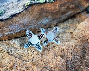 May include: A pair of silver earrings with a clear, translucent design featuring the symbol of the Zia sun, a traditional symbol of the Pueblo people of New Mexico.