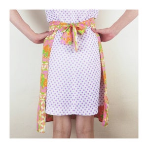 May include: A white skirt with purple polka dots and a colorful floral print on the sides. The skirt has a matching purple belt with a bow in the back.