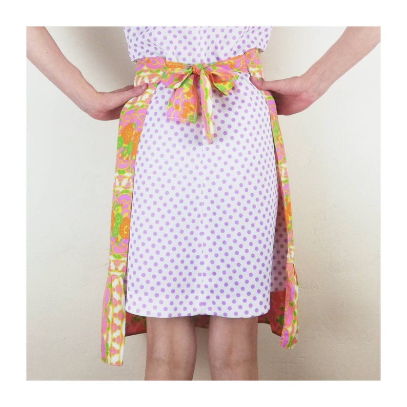 May include: A white skirt with purple polka dots and a colorful floral print on the sides. The skirt has a matching purple belt with a bow in the back.
