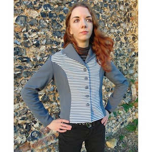 May include: A grey and white striped jacket with a collar and button fastening. The jacket has a contrasting grey fabric on the sleeves and back.