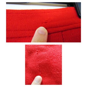 May include: Close-up of a red knitted fabric with visible stitching and small holes. The fabric is textured and has a soft appearance.