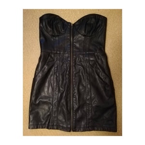 May include: A black strapless faux leather dress with a front zipper closure and two pockets. The dress has a fitted bodice and a slightly flared skirt.